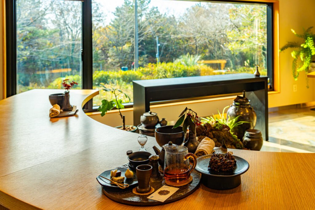 Close-up of tea being poured from a traditional ceramic pot, with Jeju citrus confections arranged on volcanic clay dishes